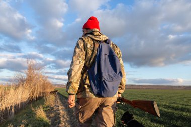 Olgun bir avcı elinde pompalı tüfekle tarlada yürüyor.