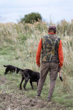 Olgun bir avcı elinde pompalı tüfekle tarlada yürüyor.