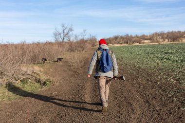Olgun bir avcı elinde pompalı tüfekle tarlada yürüyor.