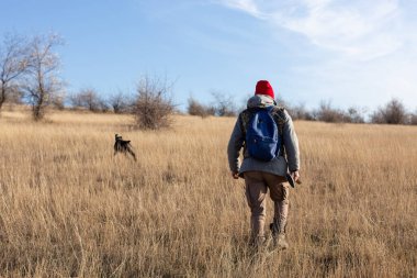 Olgun bir avcı elinde pompalı tüfekle tarlada yürüyor.