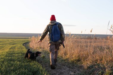 Olgun bir avcı elinde pompalı tüfekle tarlada yürüyor.