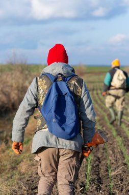 Olgun bir avcı elinde pompalı tüfekle tarlada yürüyor.