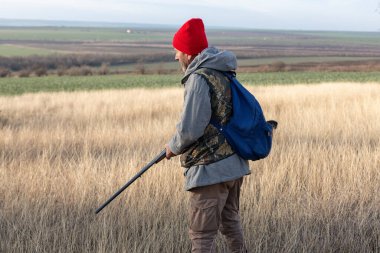 Olgun bir avcı elinde pompalı tüfekle tarlada yürüyor.