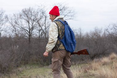 Olgun bir avcı elinde pompalı tüfekle tarlada yürüyor.