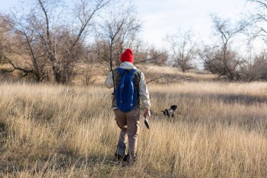 Olgun bir avcı elinde pompalı tüfekle tarlada yürüyor.