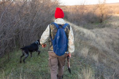 Olgun bir avcı elinde pompalı tüfekle tarlada yürüyor.