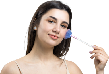 Açık renk bluzlu, beyaz arka planda yüz makyajı yapan genç bir kızın yakın çekimi. Güzel bir kadın yüzüne bir makyaj fırçası tutar ve gülümser..