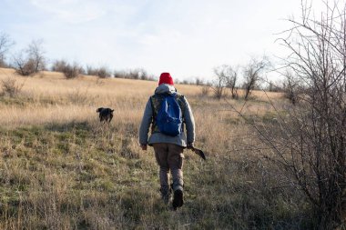 Olgun bir avcı elinde pompalı tüfekle tarlada yürüyor.