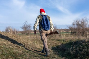 Olgun bir avcı elinde pompalı tüfekle tarlada yürüyor.