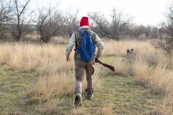 Olgun bir avcı elinde pompalı tüfekle tarlada yürüyor.