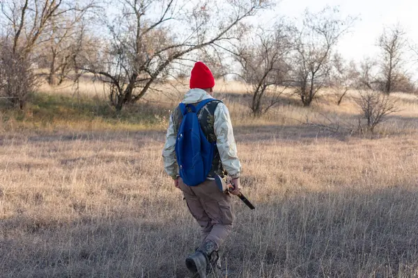 Olgun bir avcı elinde pompalı tüfekle tarlada yürüyor.