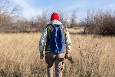 Olgun bir avcı elinde pompalı tüfekle tarlada yürüyor.