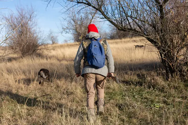 Olgun bir avcı elinde pompalı tüfekle tarlada yürüyor.