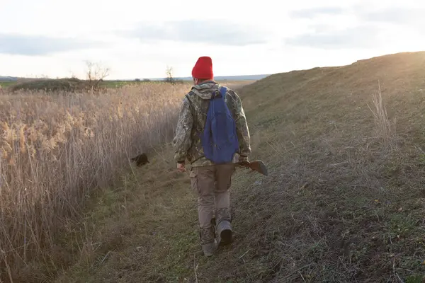 Olgun bir avcı elinde pompalı tüfekle tarlada yürüyor.