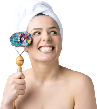 Kafasında havlu olan esmer, gri arka planda izole edilmiş yüz masajı için silindir kullanıyor.