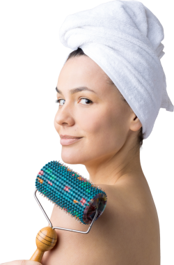 Kafasında havlu olan esmer, gri arka planda izole edilmiş yüz masajı için silindir kullanıyor.