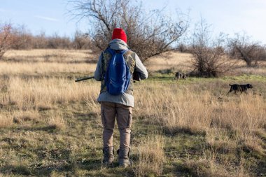 Olgun bir avcı elinde pompalı tüfekle tarlada yürüyor.