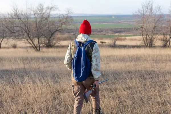 Olgun bir avcı elinde pompalı tüfekle tarlada yürüyor.