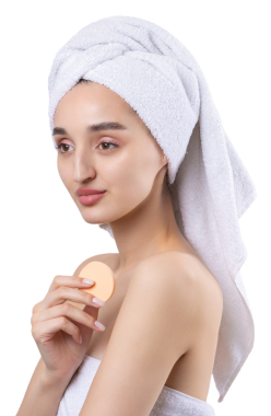 Kalın kaşlı güzel bir kız, beyaz arka planda mükemmel bir ten, kafasında havlu, güzel bir fotoğraf. Kozmetik sünger tutuyor..