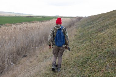 Olgun bir avcı elinde pompalı tüfekle tarlada yürüyor.