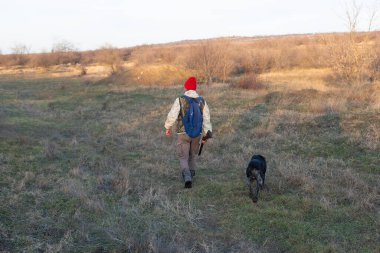Olgun bir avcı elinde pompalı tüfekle tarlada yürüyor.
