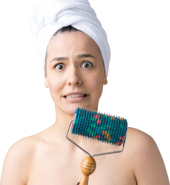 Kafasında havlu olan esmer, gri arka planda izole edilmiş yüz masajı için silindir kullanıyor.