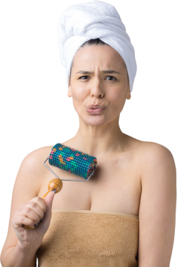 Kafasında havlu olan esmer, gri arka planda izole edilmiş yüz masajı için silindir kullanıyor.