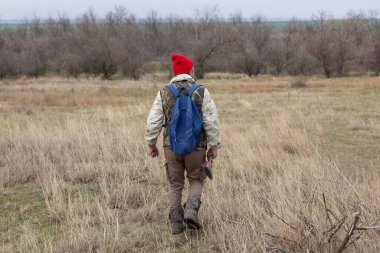 Olgun bir avcı elinde pompalı tüfekle tarlada yürüyor.