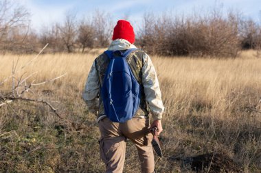 Olgun bir avcı elinde pompalı tüfekle tarlada yürüyor.