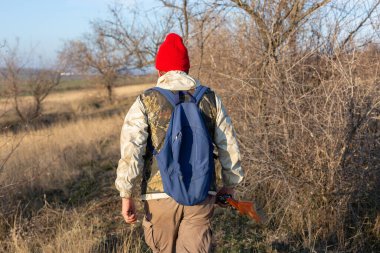 Olgun bir avcı elinde pompalı tüfekle tarlada yürüyor.