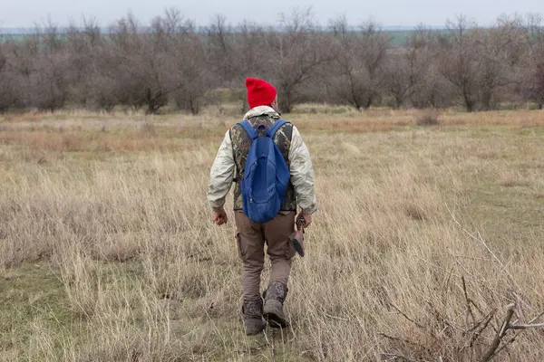 Olgun bir avcı elinde pompalı tüfekle tarlada yürüyor.