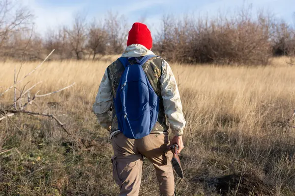 Olgun bir avcı elinde pompalı tüfekle tarlada yürüyor.