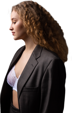 Stüdyoda uzun saçlı, ceketli, kızıl saçlı, kıvırcık bir kızın portresi. Kıvrımlı göğüslerini sütyen içinde gösteriyor..