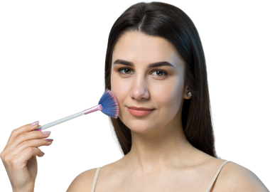 Açık renk bluzlu, beyaz arka planda yüz makyajı yapan genç bir kızın yakın çekimi. Güzel bir kadın yüzüne bir makyaj fırçası tutar ve gülümser..