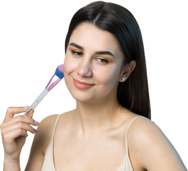 Açık renk bluzlu, beyaz arka planda yüz makyajı yapan genç bir kızın yakın çekimi. Güzel bir kadın yüzüne bir makyaj fırçası tutar ve gülümser..