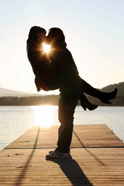 A couple kissing on a jetty by the water at sunset