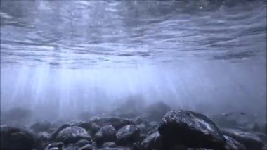 Su altı videosu, mavi sularda akmakta olan taşların ve güneş ışınlarının olduğu bir dere.