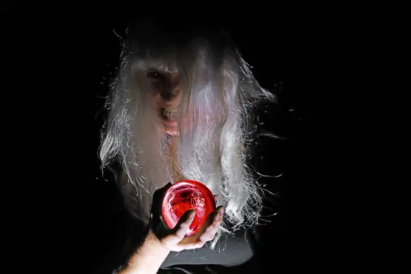 stock image A creepy white-haired old woman with a red glass ball in the light and shadows of the night