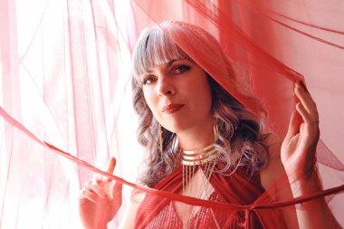 Kırmızı elbiseli güzel bir kadın perdeden bakar.