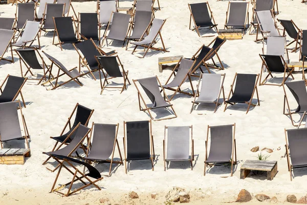 Scenic water view of many empty black wooden deckchair loungers on sand river or sea ocean beach. Rows of deckchair on closed coast due contamination. Lack of people tourist on resort due sanctions.