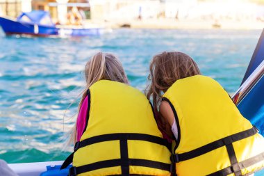 Arkaya bakan iki sevimli, küçük, mutlu, mutlu, gülümseyen beyaz kız arkadaş, açık denizde mavi su güneşine karşı yelken açmaktan zevk alırlar. Yaz tatili tatili.