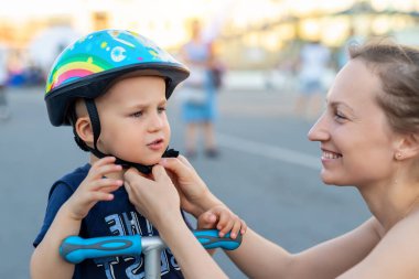 Yakın plan anne babası, yaz günü bisiklet sürdüğü ya da Scooter City Sokak Parkı 'nda gezdiği için sevimli sarışın, beyaz çocuk için kaskını takmış ve kaskını takmış. Çocuk sporları koruma hizmetleri.