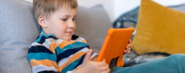 Sevimli, sevimli sarışın çocuğun portresi evde kanepede oturmaktan, internette sörf yapmaktan ya da tablet kullanarak TV dizisi filmleri izlemekten zevk alıyor. Çocuklar akıllı teknoloji kullanımı konsepti. Çocuk aleti bağımlılığı.
