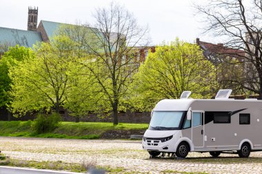 Many white modern campervan recreational motor home vehicles parked in row at camper park site Magdeburg city against Elbe river bridge. Motorhome campground stataion travel destination. RV lifestyle.