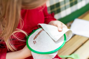 Close-up detail female child hands embroidering round hoop fabric frame with cross-stitch . Girl person handmade craft sewing pattern on canvas. Children development fine motor skills hobby artwork.