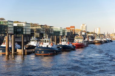 Günbatımında Hamburg Elbe limanında birçok modern güçlü çekici servis ekibi sıraya dizildi. Almanya endüstriyel kargo nakliye limanındaki römorkör filosunu destekleyin..