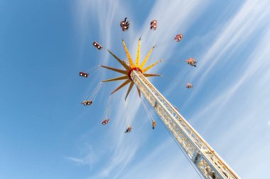 Manzaralı alt manzara yüksek zincirli salıncak mavi gökyüzüne doğru uçan atlıkarınca. Merry, portatif lunaparktaki şöförlü uçağın etrafından dolaş. İnsanlar panayır festivalinde aile eğlencesine binmekten hoşlanıyor..