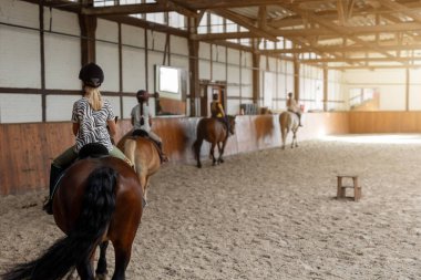 Ata binme kursu. Grup halinde binicilik dersleri alan küçük çocuklar çiftlik atı binicilik salonunda. Şirin, yeni başlayan, kasklı sarışın kız, kahverengi at sırtında oturuyor..