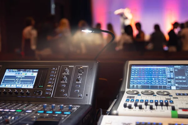 Live theater concert show sound video music control console with scene lights background. Sound engineer mixer soundboard equipment with many knobs, buttons, faders, equalizer screen and light.