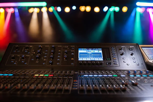 Live theater concert show sound video music control console with scene lights background. Sound engineer mixer soundboard equipment with many knobs, buttons, faders, equalizer screen and light.
